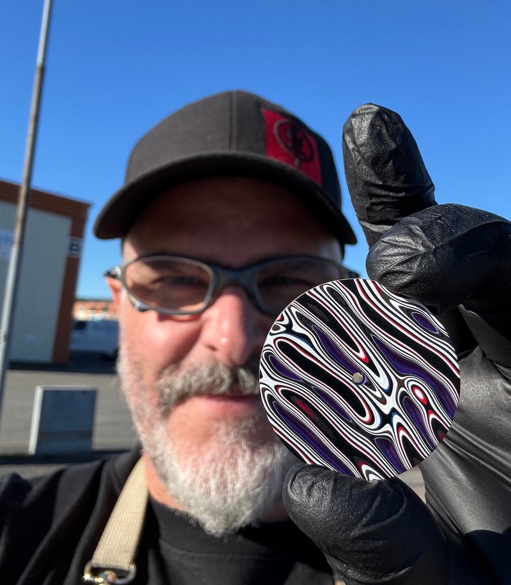 James Thompson, AKA Black Badger, holding up a finished Arcanaut Fordite dial to camera.